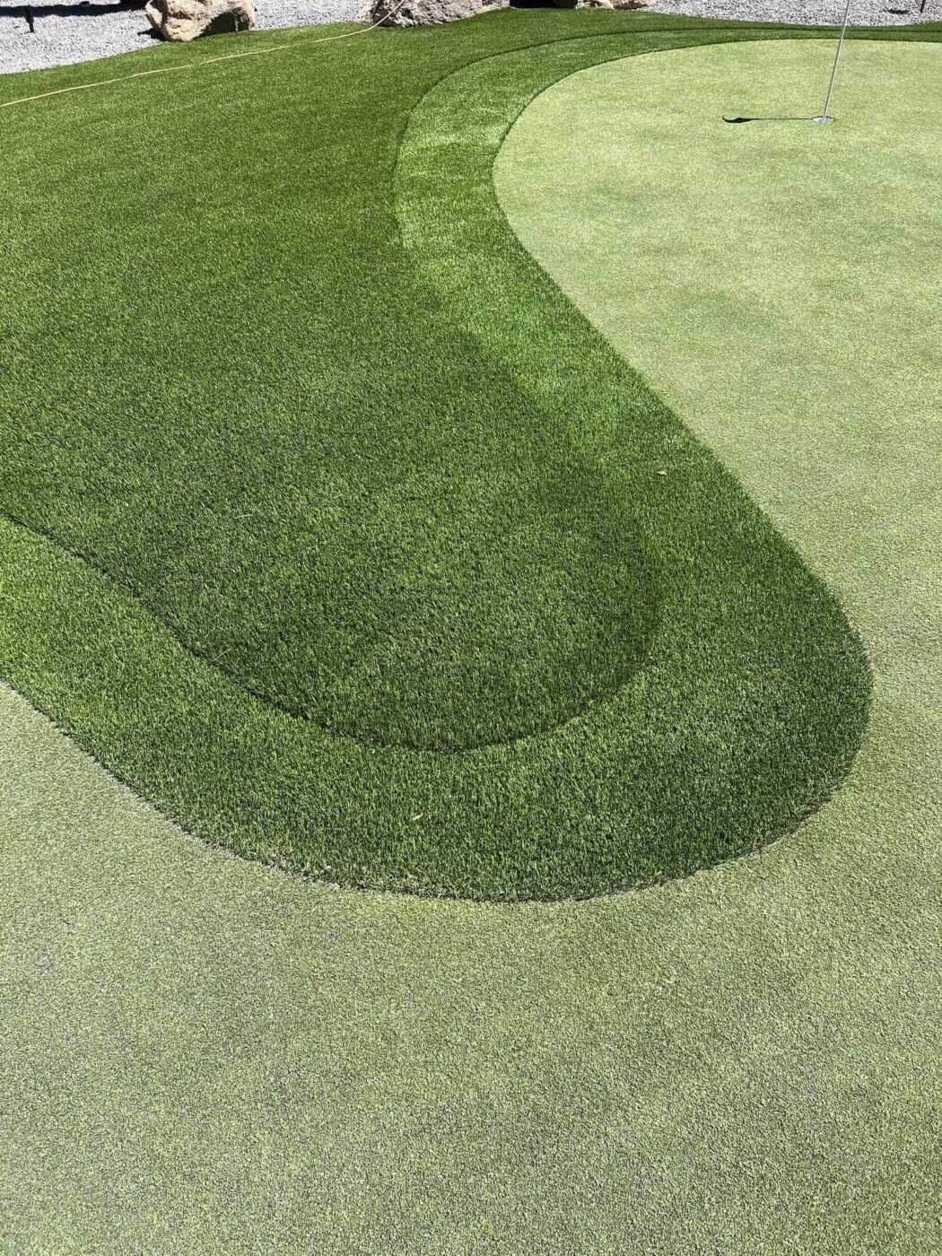 A close-up of a backyard putting green with neatly trimmed artificial turf, showing various shades of green and a small golf flag in the hole—perfect for practicing your short game after an expert artificial grass installation.